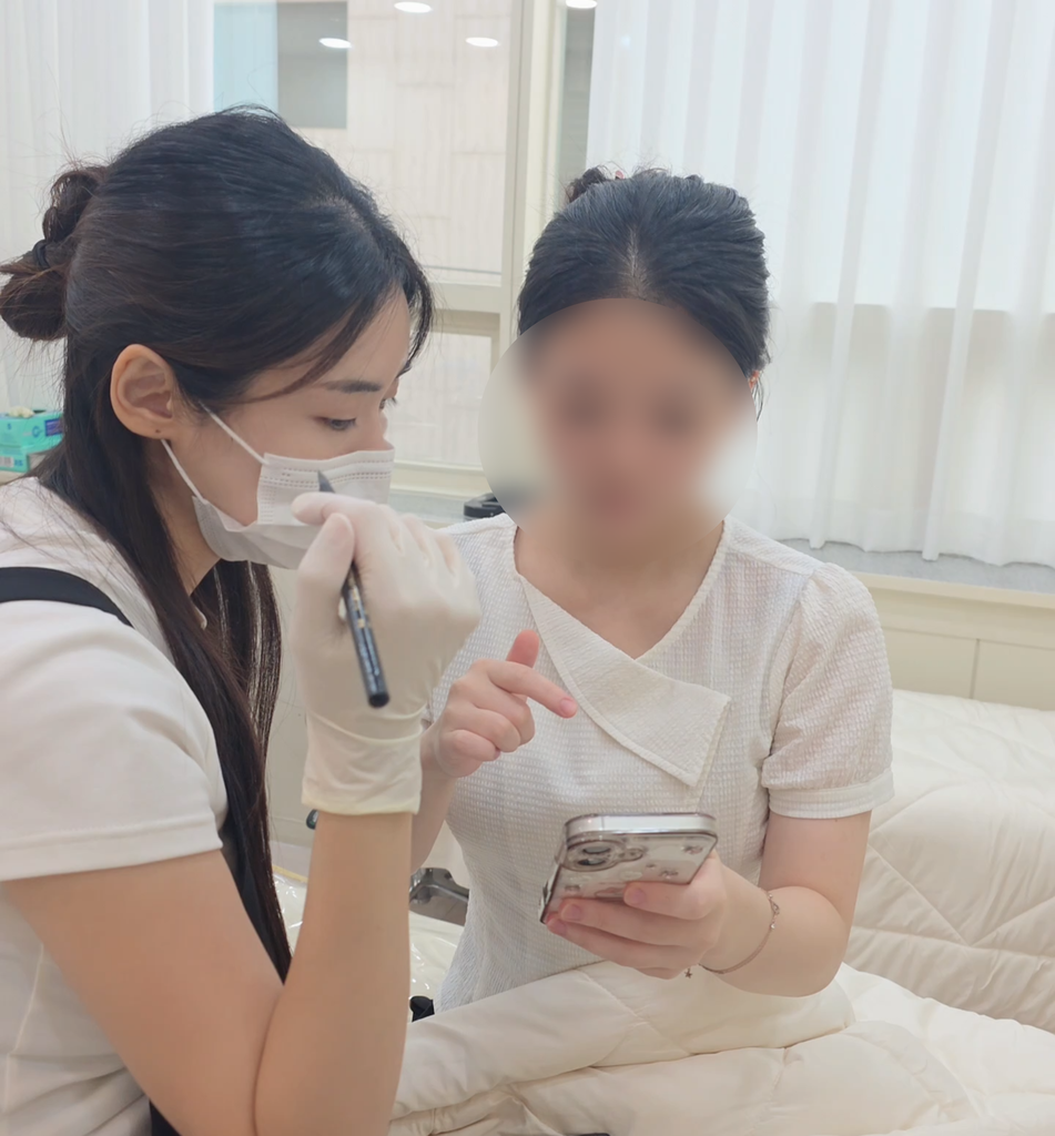携帯電話の参考写真を見せながら眉のデザインを相談する様子
